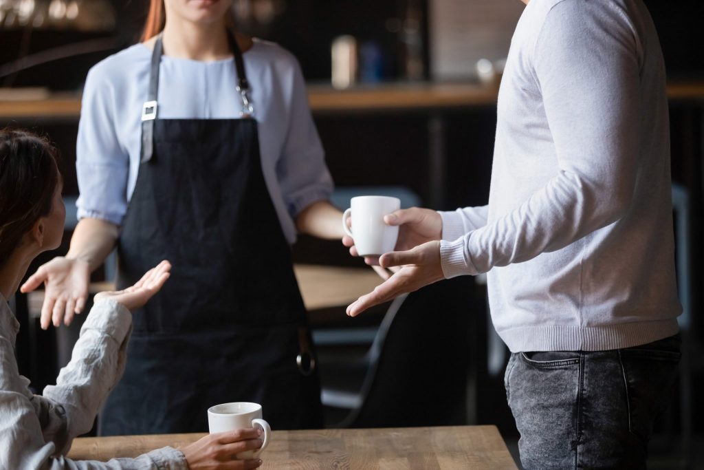 Two people talking to the waiter at a coffee shop.