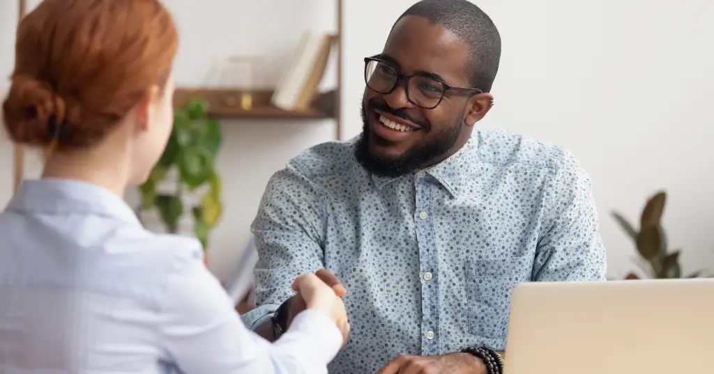 A man and a woman engaging in a strategic handshake in front of a laptop, initiating action by strategically distributing high-impact data.