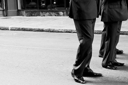 Legs of group of men standing on a street.