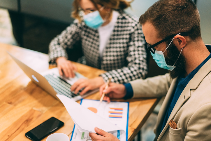 Two people wearing face masks working at a desk.