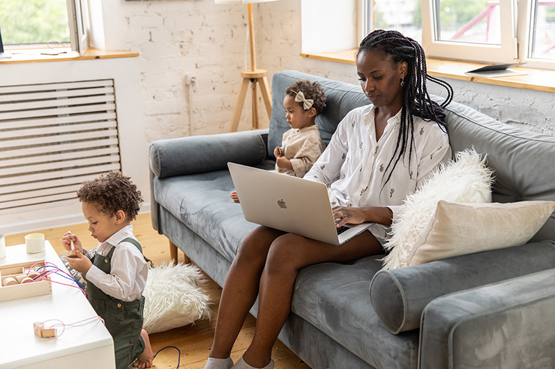 A woman working on a laptop in her living room with her children.